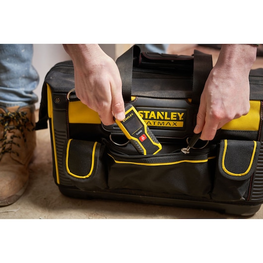 STANLEY FMST1-71180 bag with yellow and black design, front pocket unzipped, person inserting STANLEY tool.