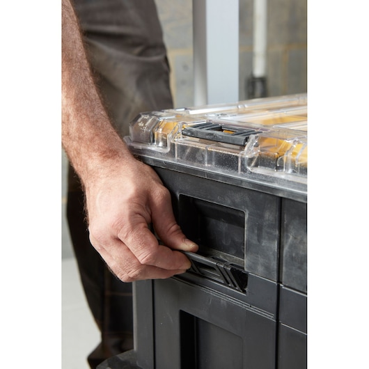 STANLEY FMST1-71970 storage box close-up, hand unlocking black latch, transparent lid visible.
