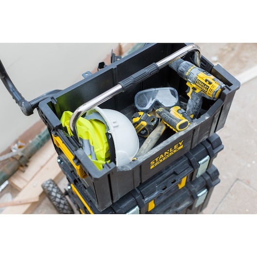 STANLEY FMST1-75677 stackable toolbox open top, showing tools, hard hat, goggles, and drill on a worksite.