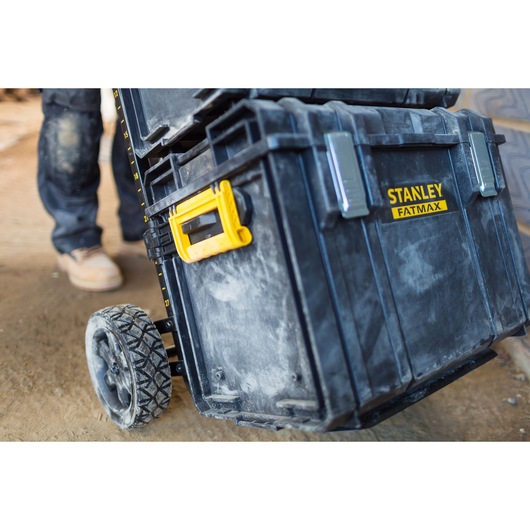 STANLEY FMST1-75682 black wheeled tool box with yellow handle, close-up on construction site.