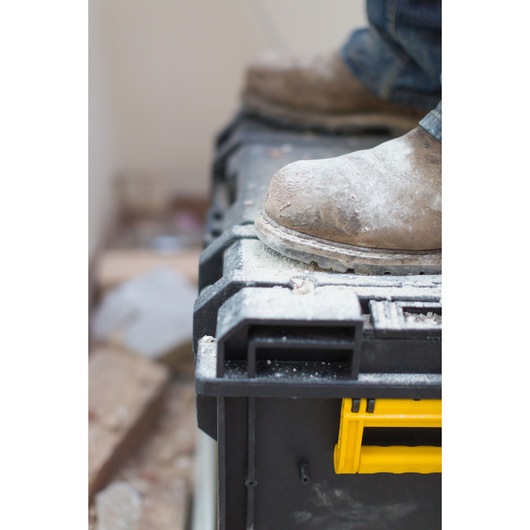 STANLEY FMST1-75682 toolbox with yellow handle, dusty work boots standing on top, close-up side angle.