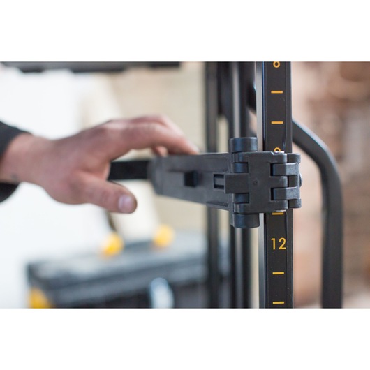 STANLEY FMST1-75684 close-up, hand adjusting black folding stand arm with yellow measurements.