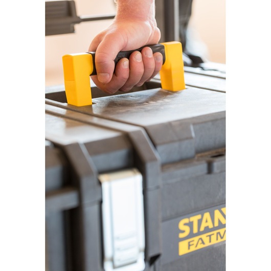 Photo of STANLEY FMST1-75798 toolbox being carried by a hand, showing the yellow and black handle close-up.