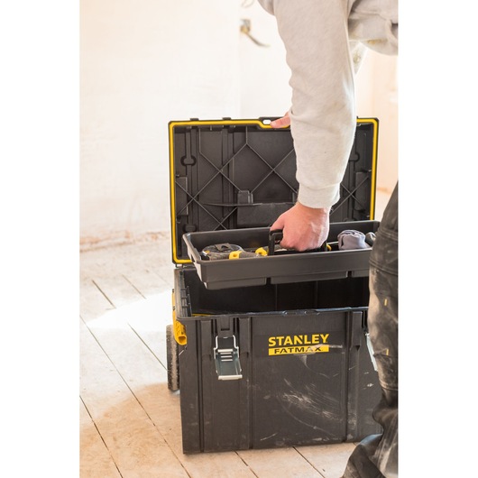 STANLEY FMST1-75798 tool box with open lid, person lifting the tray, shown indoors on wooden floor.