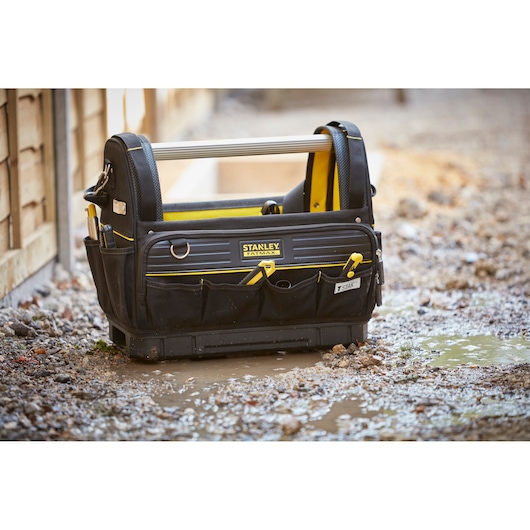 STANLEY FMST83296-1 tool bag with handle and pockets, black and yellow, on wet construction ground.