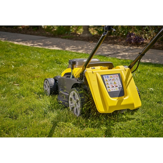STANLEY SCMWP3701N lawn mower side view on grass, yellow body, warning label visible, large rear wheels.