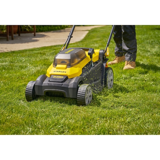 STANLEY SCMWP3701N lawn mower in yellow and black, shown in use on grass, with visible cuttings and user’s legs.