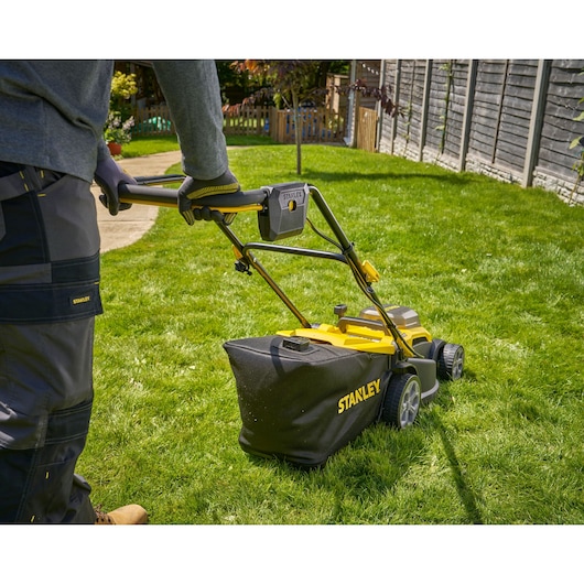 Photo of STANLEY SCMWP3701N cordless lawn mower in use on a grassy backyard, rear angle showing collection bag.