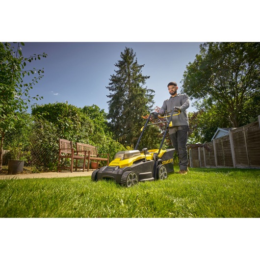 STANLEY SCMWP3701N lawn mower in use on grass in a garden, person pushing mower, photographed outdoors.