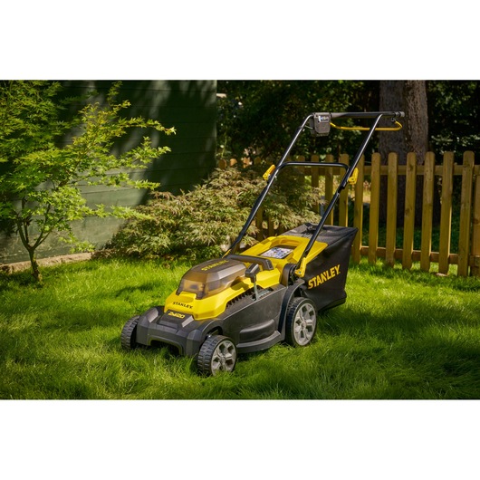 STANLEY SCMWP3701N lawn mower in yellow and black on grass with fence and foliage in background.