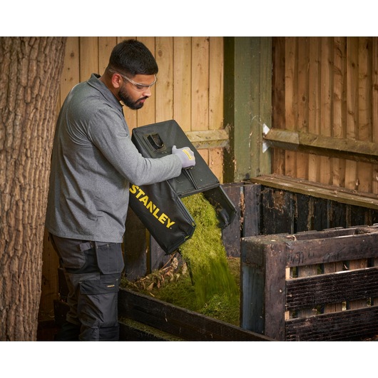 STANLEY SCMWP3701N lawn mower grass bag emptied into wooden compost bin, outdoor setting.