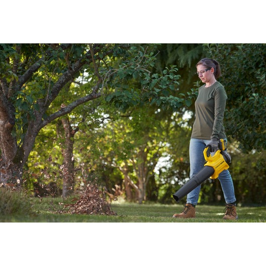 STANLEY SFMCBL730M1 leaf blower in use outdoors, yellow and black handheld cordless tool blowing leaves.