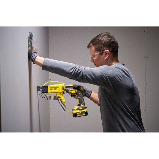 Person using STANLEY SFMCF600B cordless autofeed screwdriver with screw strip on drywall.
