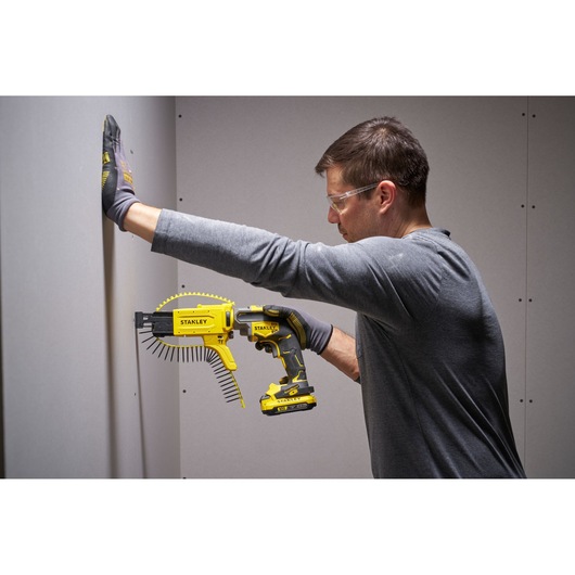 Stanley SFMCF600B cordless screw gun being used by a person to fasten drywall, side view.