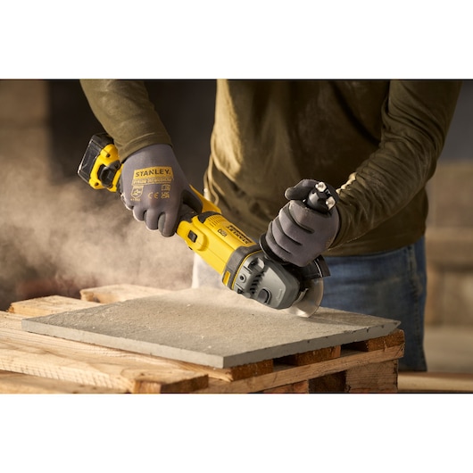 STANLEY SFMCG300B angle grinder cutting concrete slab, worn by worker with gloves.