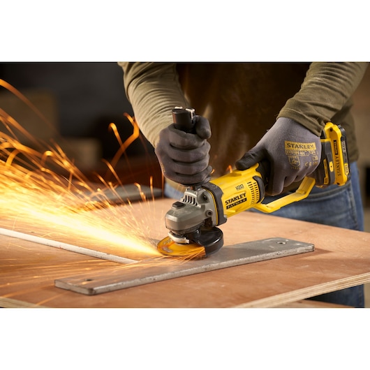 Photo of STANLEY SFMCG300B angle grinder in use, grinding metal with sparks, worker wearing gloves.
