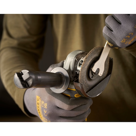 STANLEY SFMCG300B angle grinder held in gloved hands, close-up showing accessory change.