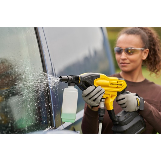 STANLEY SFMCPC93M1 portable power cleaner spraying water on a car window in an outdoor setting.