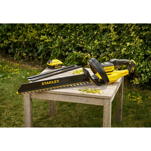 Stanley STCHT8255M1 hedge trimmer with battery on wooden table outdoors, black and yellow design.