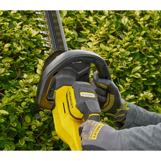 STANLEY STCHT8255M1 hedge trimmer in use trimming green bushes, close-up photography of handle and blade.