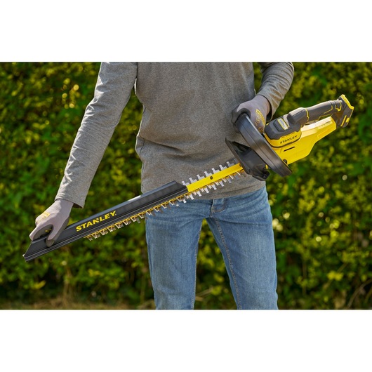 STANLEY STCHT8255M1 hedge trimmer, yellow and black, shown in use outdoors.
