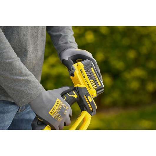 Photo of STANLEY STCHT8255M1 gloves holding a yellow 18V power tool outdoors.