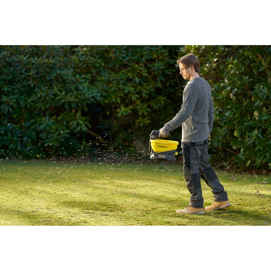 STANLEY STCOE300D1 handheld spreader in use outdoors, spreading material on a grassy lawn.