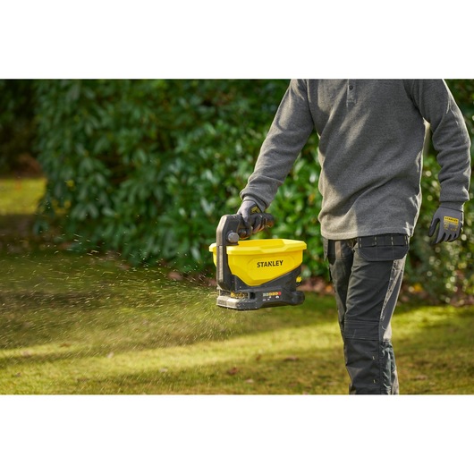 STANLEY STCOE300D1 handheld spreader in use on grass lawn outdoors, yellow and black design.