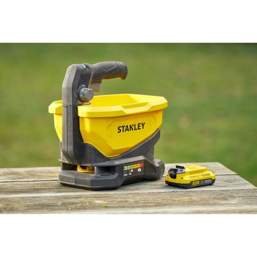 STANLEY STCOE300D1 yellow cordless spreader and battery on wood table, side angle outdoor.