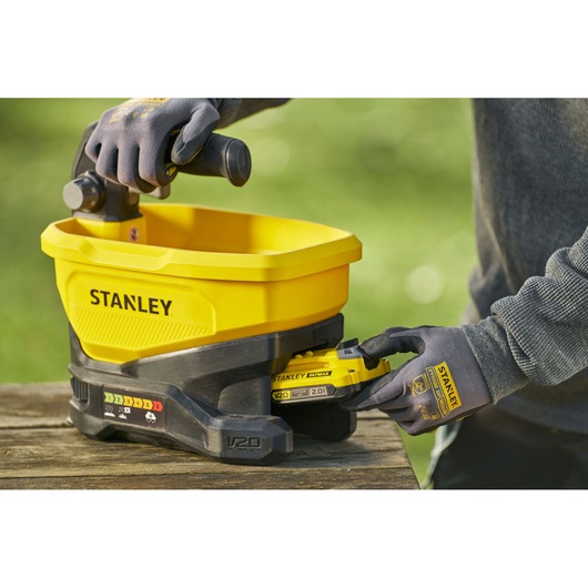 STANLEY STCOE300D1 yellow cordless spreader on wood table, side angle, with V20 battery being inserted.