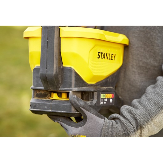 Stanley STCOE300D1 yellow spreader held by gloved hand, outdoor close-up view.