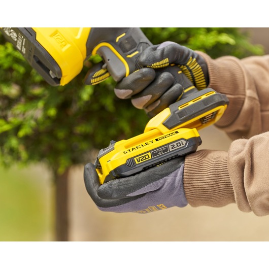 STANLEY STCSS20D1 V20 cordless power tool battery held by gloved hands outdoors.