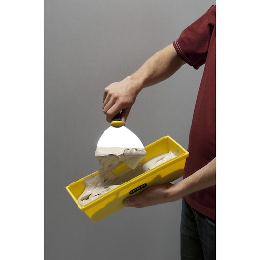 STANLEY STHT0-05866 yellow mud pan with joint compound and putty knife, hand-held, side view.