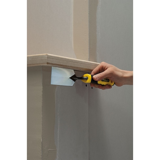 STANLEY STHT0-05896 paint scraper with yellow handle used on wall corner, close-up photography.