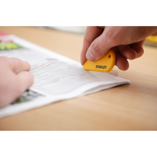 Photo of STANLEY STHT0-10291 yellow safety cutter used to slice paper on a desk.