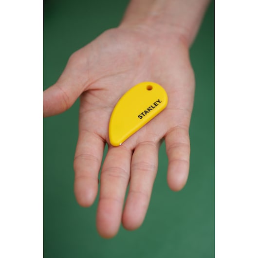 STANLEY STHT0-10291 yellow plastic key-shaped scraper held in a hand, product photography.