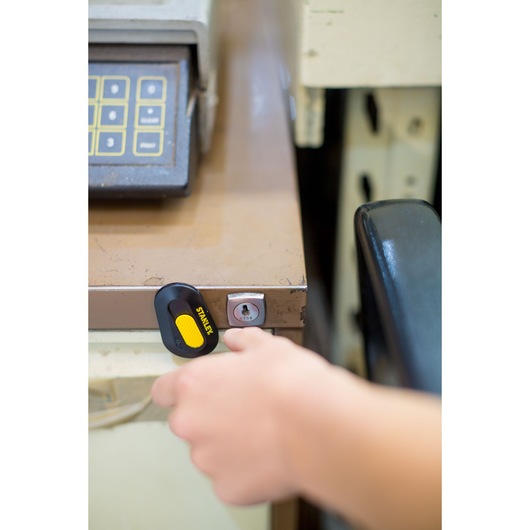 STANLEY STHT0-10292 utility knife with yellow slider held near a drawer lock, photographed from an overhead angle.