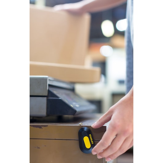 STANLEY STHT0-10292 utility knife magnetically attached to metal cabinet, hand reaching for it, indoor setting.