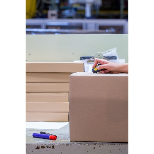 STANLEY STHT0-10292 utility knife used to cut box tape on a cardboard parcel, close-up angle.