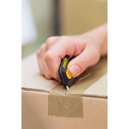 Photo of STANLEY STHT0-10292 utility knife cutting tape on cardboard box, handheld, product in use.