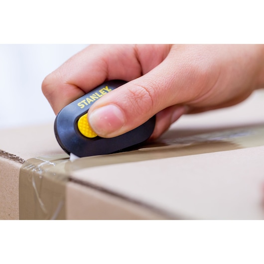 STANLEY STHT0-10292 compact box cutter in hand opening a taped cardboard box, close-up.