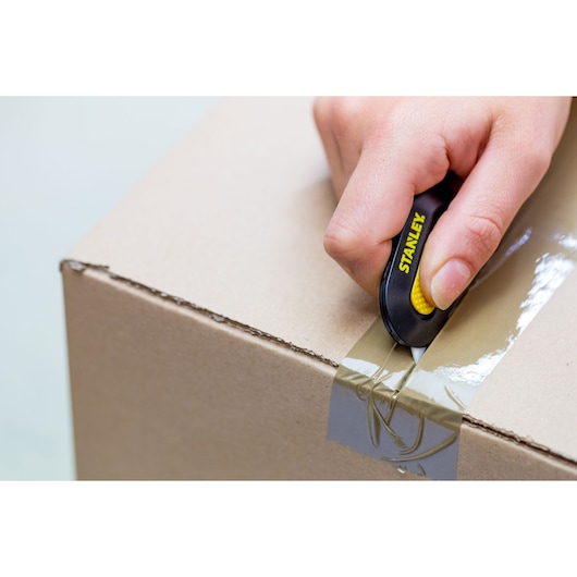 STANLEY STHT0-10292 utility knife cutting tape on a cardboard box, close-up view.