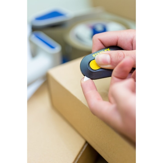 Photo of STANLEY STHT0-10292 safety cutter in hand, cutting cardboard box, close-up view.