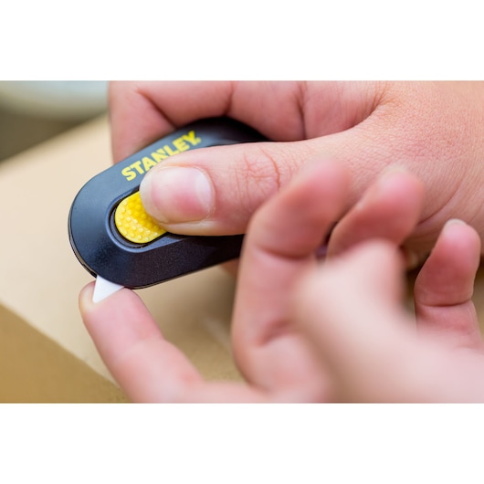 Photo of STANLEY STHT0-10292 utility knife with yellow button, held in hand, cutting cardboard.