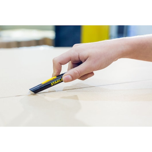 STANLEY STHT0-10293 utility knife cutting cardboard, close-up of hand holding black and yellow knife.