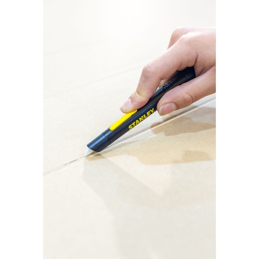 Photo of STANLEY STHT0-10293 utility knife cutting cardboard, black and yellow handle visible in hand.