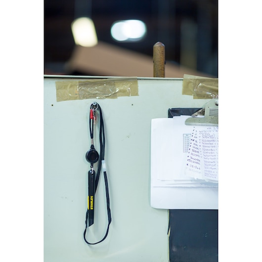 STANLEY STHT0-10293 black lanyard utility tool hanging on wall next to clipboard with papers, front angle.