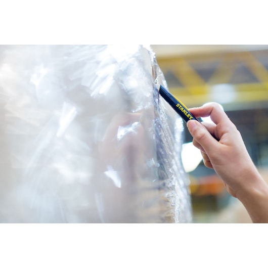 Close-up of hand using STANLEY STHT0-10293 utility knife to cut plastic wrap, photography.