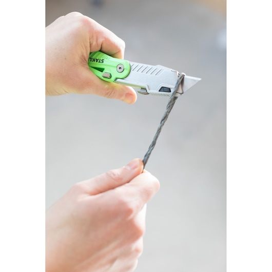Photo of STANLEY STHT0-10823 utility knife cutting a wire, close-up showing green and silver handle.