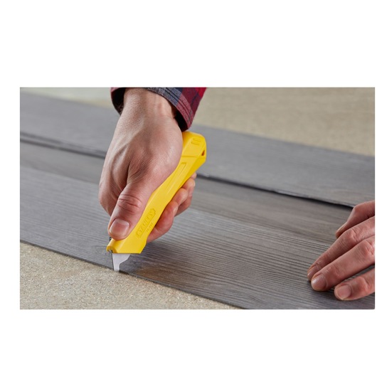 STANLEY STHT0-11941 yellow utility knife cutting grey laminate flooring, close-up action photography.
